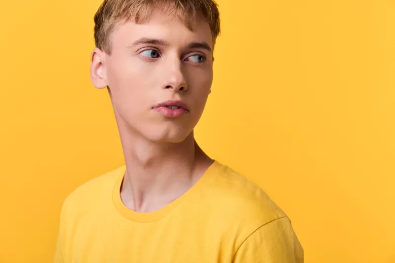 Man in a yellow t-shirt against a bright backdrop, looking to the side, showcasing studio fashion with clean lighting, minimal background, casual mood, contemporary youth style for apparel and