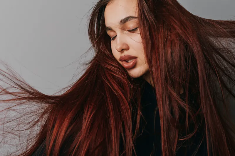 Woman with long red hair and closed eyes posing in studio, natural makeup and smooth skin with flowing hair strands for beauty and fashion portrait.