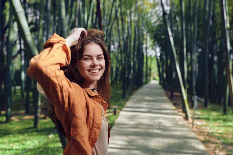 Woman smile park path trees outdoor portrait nature happy casual young female smiling on a tree-lined walkway, enjoying sunlight and leisure, lifestyle, travel and relaxed mood.