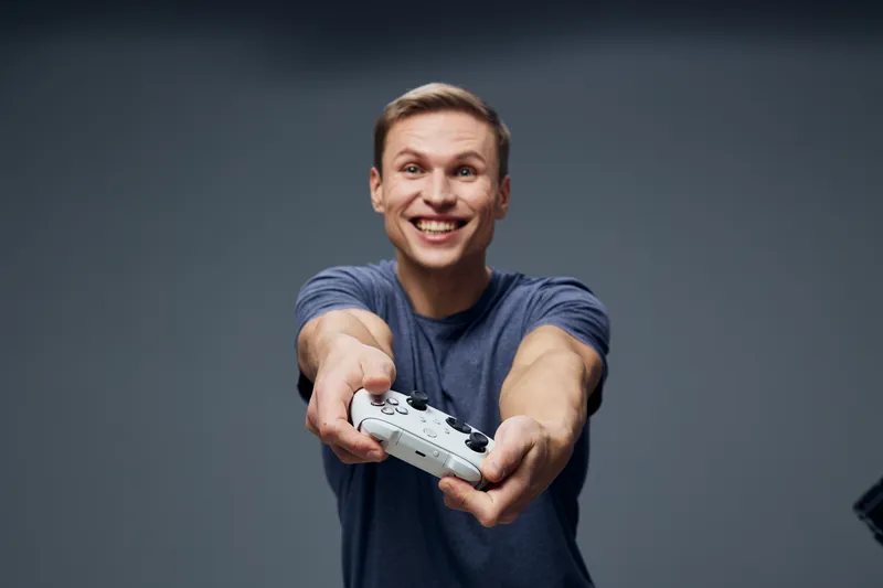 Smiling young caucasian man holding gaming joystick looking camera wearing casual t-shirt isolated on gray background lifestyle concept play video game happy