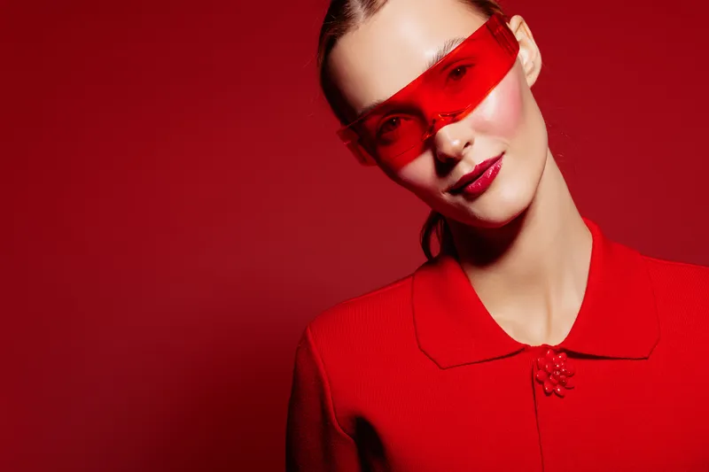 Young woman in red outfit and red sunglasses poses against red background. Fashion portrait with vibrant colors and confident expression. Concept of style, modernity, and boldness.