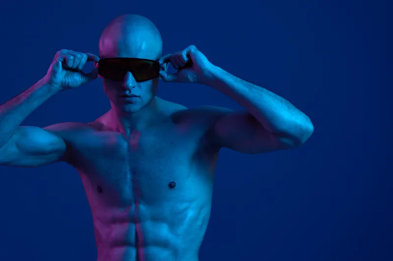 Athletic man adjusting sunglasses against a vivid blue background. The image features a strong pose and an eye-catching color palette, evoking confidence and style.