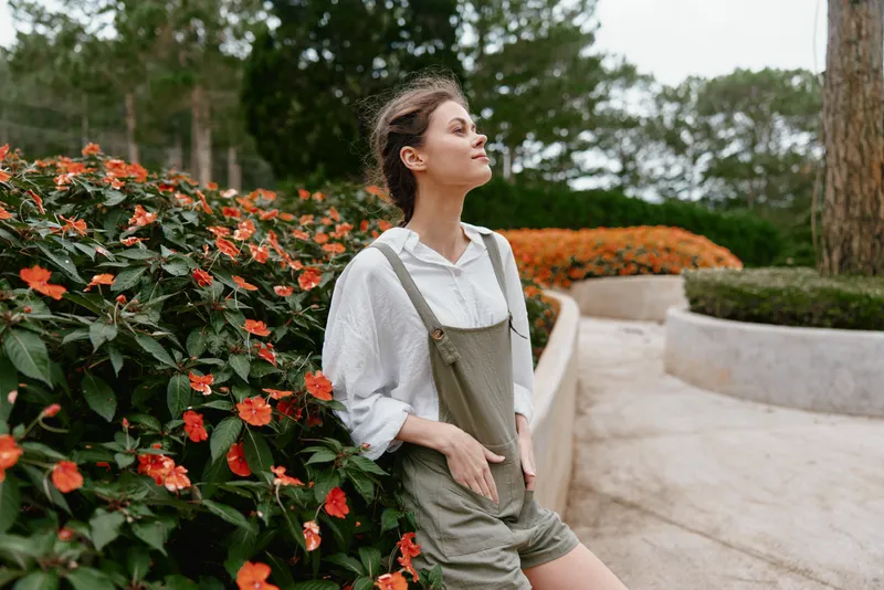 Young woman in casual outfit enjoying a serene moment in a blooming garden with vibrant flowers, exuding calmness and gratitude in nature