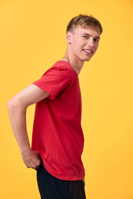Youth with a bright smile poses in a red shirt against a bold yellow background, showcasing casual style and confident energy for fashion, lifestyle and promotional campaigns