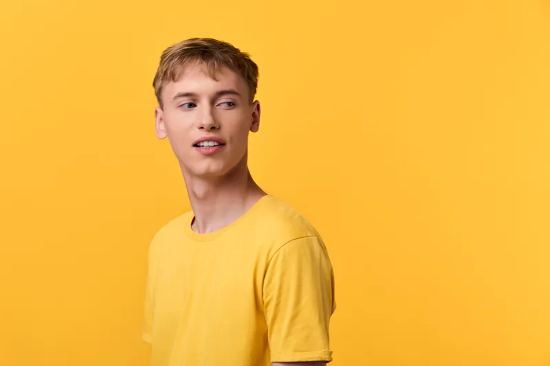Young man in a yellow t shirt against a bright yellow backdrop, casual studio shot highlighting sunny mood, relaxed expression and fashion lifestyle appeal for marketing