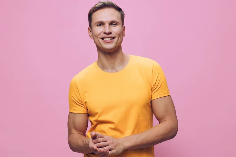 Smiling young man with short hair wearing bright yellow t-shirt posing cheerful against pink background, relaxed body language, friendly expression, studio portrait, casual style, people concept