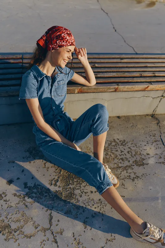 Lifestyle woman in modern boho-western denim street style sitting outdoors wearing a red bandana with a relaxed and sunny film color aesthetic.