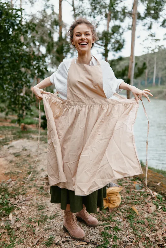 Cheerful woman in a beige apron enjoying nature, showcasing a joyful lifestyle with a rustic background and earthy color palette Seasonal, organic vibe