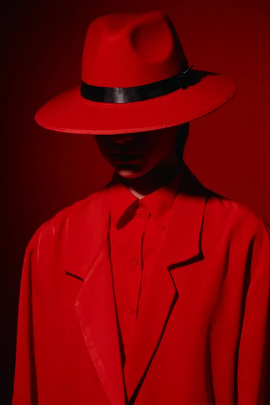 Stylish woman dressed entirely in red wears a wide-brimmed hat and coat, with the shadow obscuring her face. Concept of creative fashion, bold style, and beauty editorial.