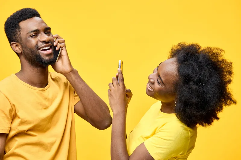Happy young couple talking and taking selfies against a vibrant yellow background, showcasing joy and connection in casual summer attire