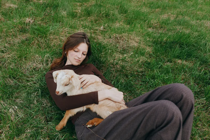 Young woman lies on green grass, embracing a light brown dog, enjoying a peaceful outdoor moment, casual cozy lifestyle, affectionate bond, sunny relaxed mood, candid portrait in nature