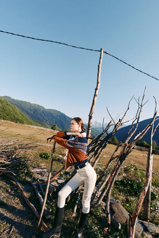 Woman mountain fence field landscape sweater boots rural portrait of a young female leaning on a rustic wooden fence in an open mountain field wearing knit sweater and boots.