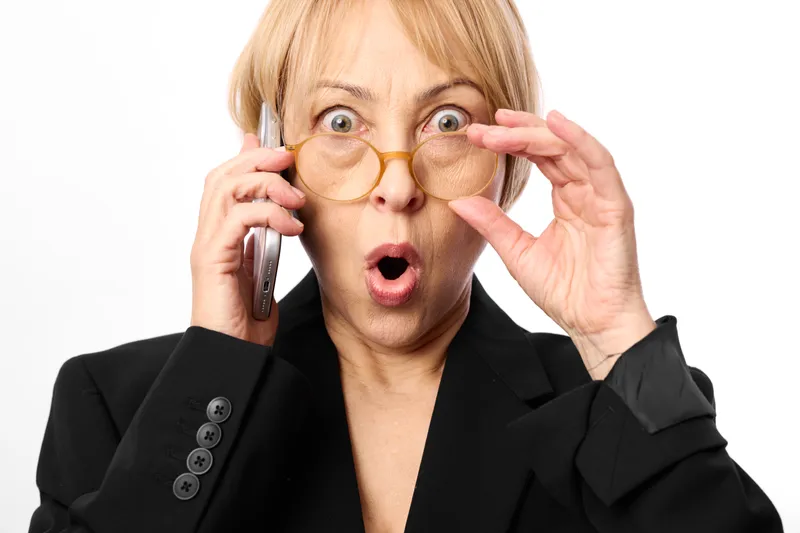 Surprised woman applying beauty makeup pads under eyes, holding phone near ear, closeup studio portrait on white background, skincare routine shows multitasking, focus moment today