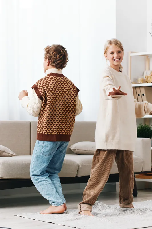 A candid indoor scene showcasing authenticity as siblings dance in a cozy living room, capturing playful movement and daily lifestyle with a hint of school age energy.