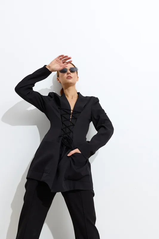 Fashion woman dressed in stylish black outfit posing confidently against white background with sunglasses, showcasing modern elegance and bold attitude in bright daylight.