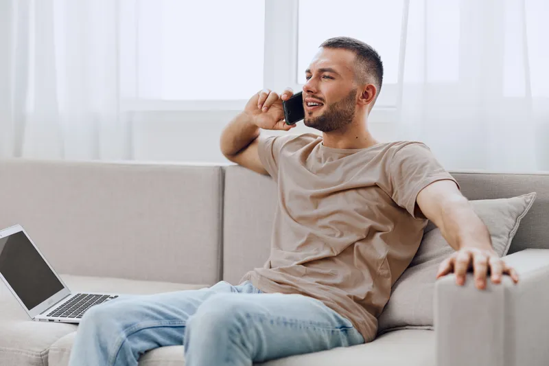 A relaxed man talking on the phone while sitting comfortably on a couch, symbolizing the blend of personal and professional life amidst digital detox.