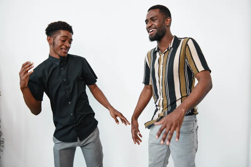 Two African American men with dark skin dancing and smiling together in casual clothes against white background. Friends enjoying leisure time and positive mood indoors.