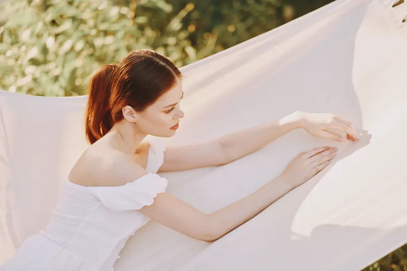 Young woman in a white dress relaxes on a hammock in nature, showcasing serenity and grace with soft lighting and a pastel background