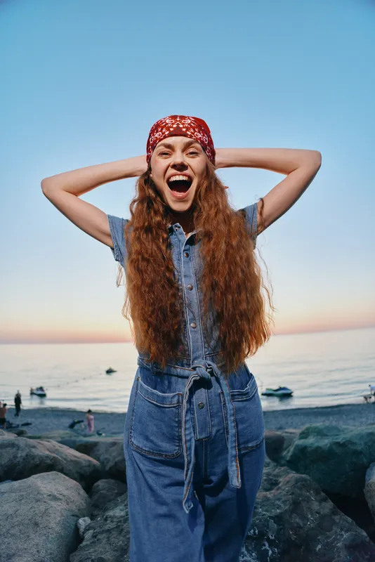 energetic woman in modern boho-western denim street style laughing joyfully outdoors with film color effect, casual summer outfit, natural light, vibrant mood