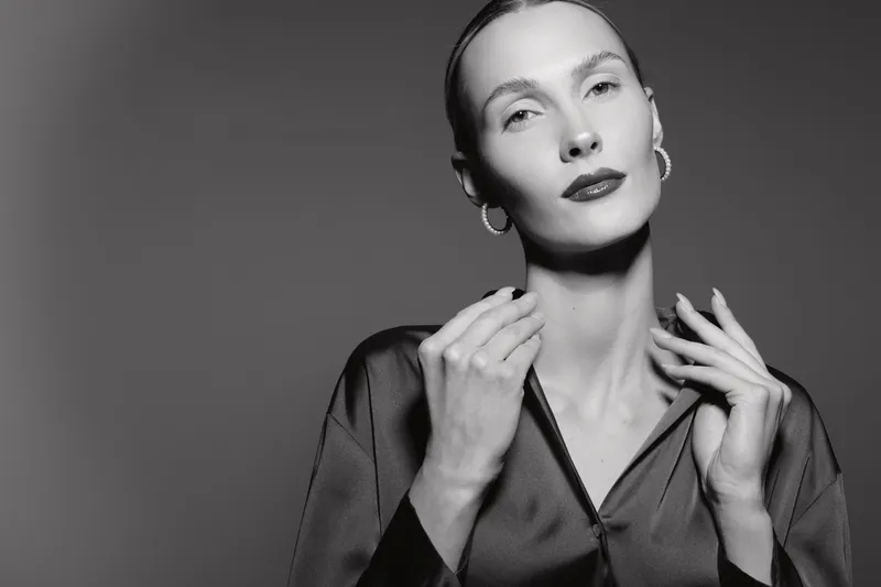 Portrait of a pale skin caucasian woman in satin blouse with hoop earrings posing in studio. Concept of elegance, fashion, and minimalistic beauty.