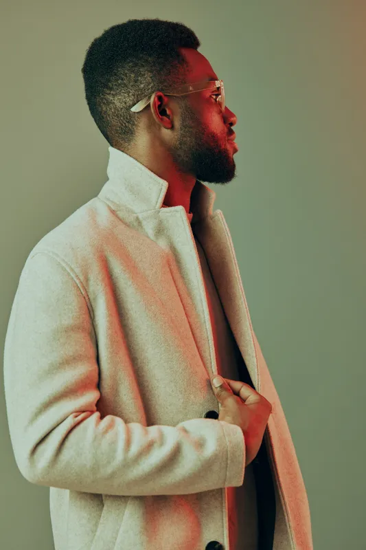 Stylish African man in a light coat showcasing confidence and modern fashion against a colorful backdrop Emphasizes contemporary style and individuality