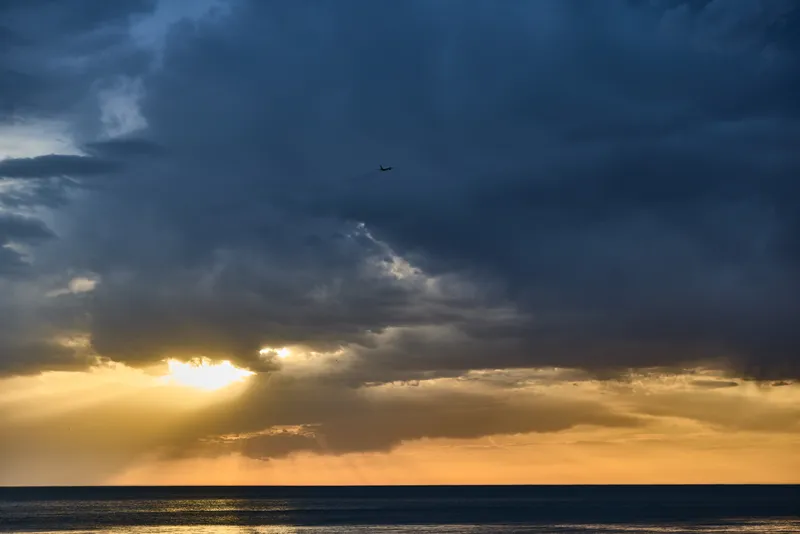 dramatic sunset over calm ocean with dark storm clouds and airplane flying above the horizon sky scenic peaceful atmosphere