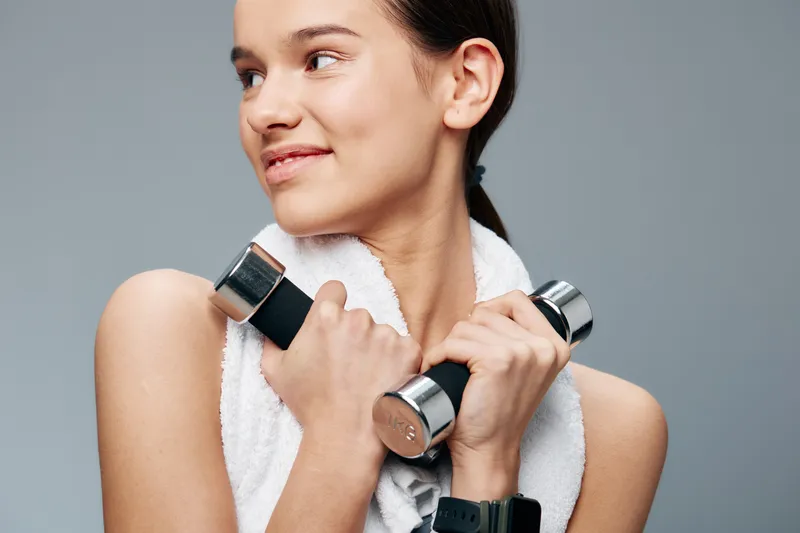 Woman fitness, sport training with dumbbells and towel, exercising in studio. Athletic pose, focused expression, gym vibe with modern equipment and steady effort.