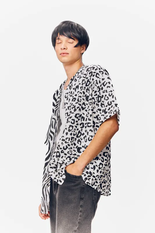 young man with closed eyes wearing a patterned shirt and jeans on a white background, casual style, relaxed mood, minimalistic composition