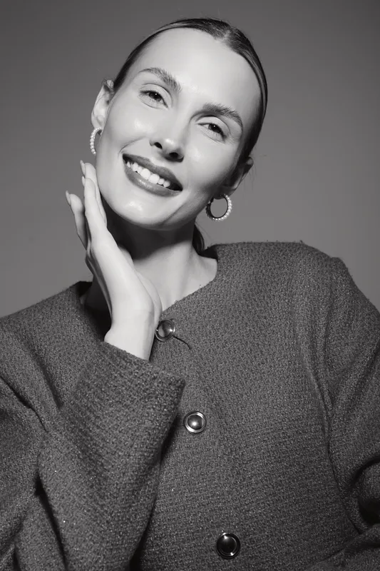 Young Caucasian woman with fair skin smiles gently, touching her face in a studio portrait. Concept of beauty, skincare, and positive expression.