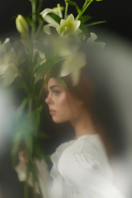 A delicate young woman in a white dress holding lilies, with a soft focus effect creating a dreamy atmosphere, perfect for concepts of beauty and nature