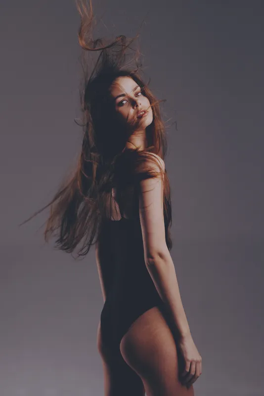 Young woman with long hair in black bodysuit posing with motion effect against grey background