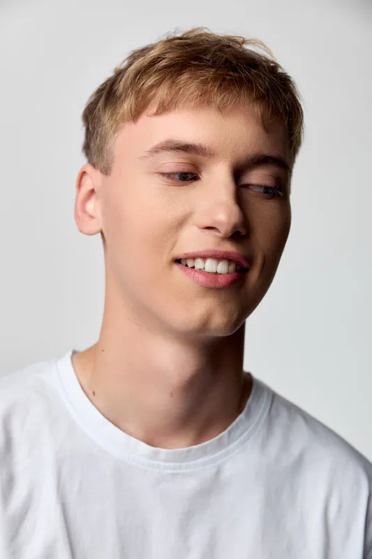 Smile, youth, young man in casual wear with white tee under soft lighting, relaxed pose and gentle expression offering approachable lifestyle and fashion stock imagery for marketing use