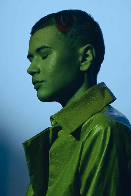 serene woman with short hair and unique hairstyle wearing green textured jacket with soft lighting and blue background in modern portrait style
