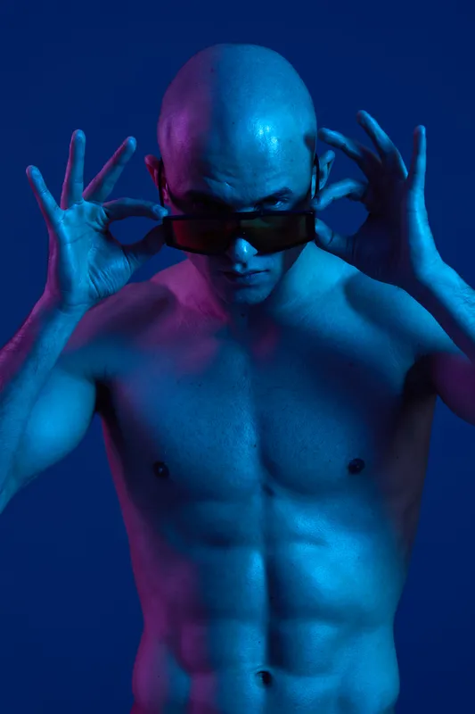 Confident man with sunglasses striking a pose, showcasing vibrant blue and purple light effects. Strong presence highlighted with a stylish edge.