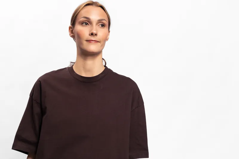 Young woman with light skin and blonde hair wearing dark brown oversized sweater looks away thoughtfully on white background. Concept for fashion, casual wear, and lifestyle portrait.