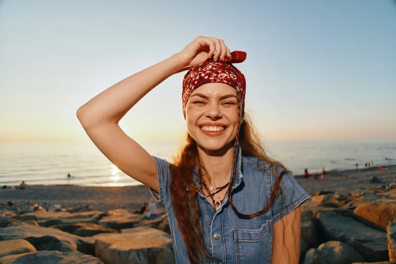 Lifestyle woman in modern boho-western denim street style smiling outdoors near the ocean at sunset with film color warmth and vibrant natural light