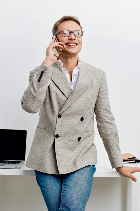 Confident smiling woman talking on mobile phone during work in office, casual stylish outfit, modern workspace background, natural light, professional communication concept