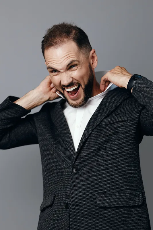A business professional stands against a solid colored background, isolated and clear. He wears a textured blazer and shows vibrant emotion, conveying energy and confidence for success.