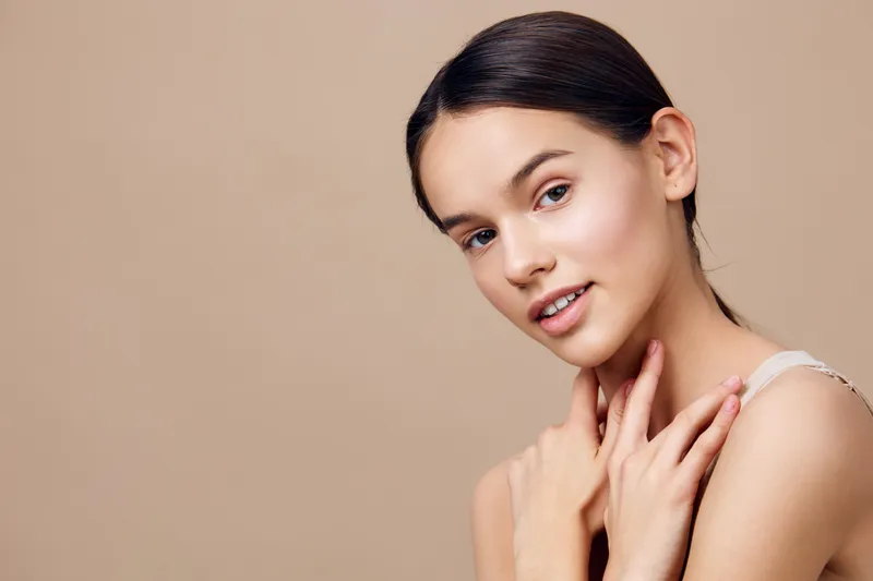 Beautiful young woman with a serene expression, showcasing healthy skin tone and natural beauty on a neutral beige background, perfect for skincare concepts