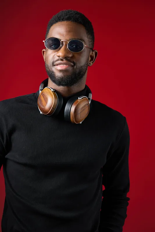 Stylish young man with sunglasses and headphones poses against a vibrant red background, showcasing a modern and trendy urban vibe ideal for music and lifestyle themes