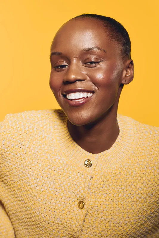 Smiling black African woman with dark skin wearing yellow knitted sweater on yellow background. Portrait of happy female model with natural makeup and positive confident mood.
