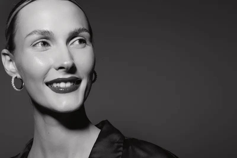 Smiling Caucasian woman with fair skin and earrings looks away in black and white portrait, elegant and confident mood.