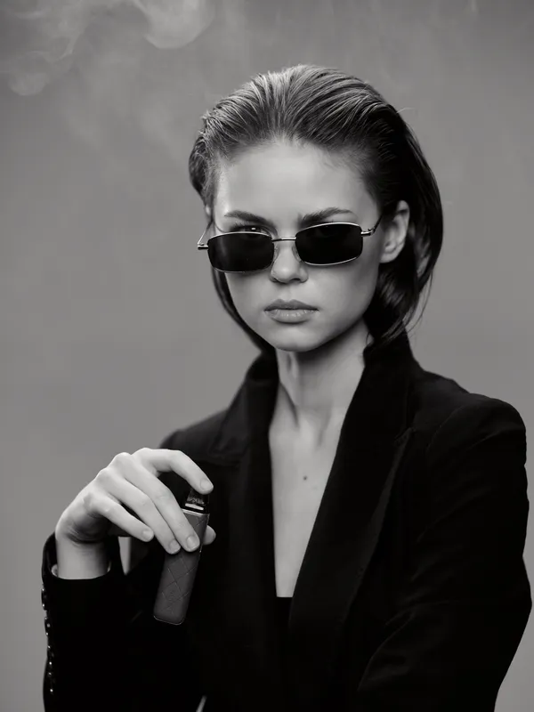 Stylish woman wearing sunglasses in black and white portrait with smoke background, fashionable look, confident expression.