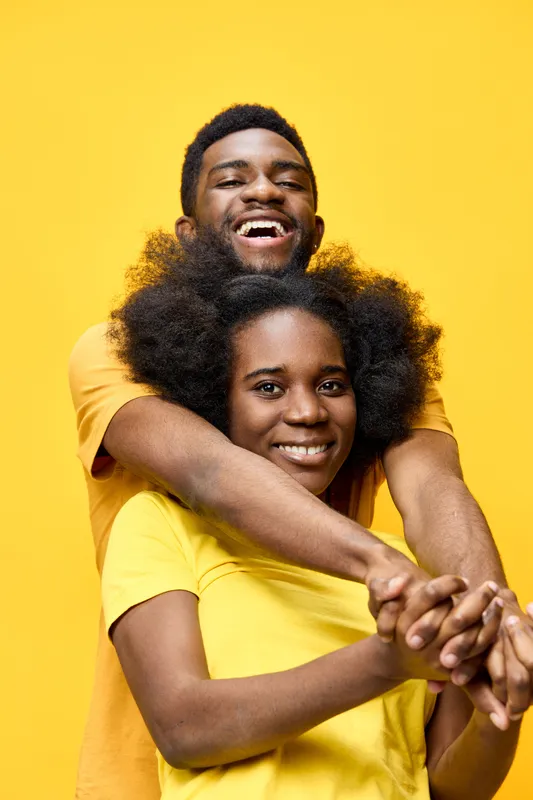 A joyful African American couple embracing against a bright yellow background, wearing matching yellow shirts, conveying happiness and togetherness in a vibrant setting