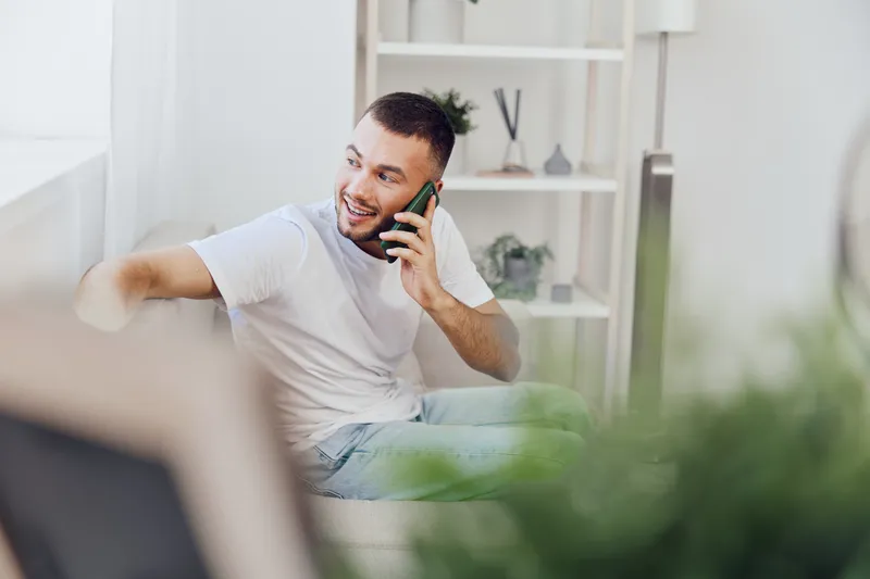 Smiling man on the phone enjoying authentic conversations, promoting emotional minimalism and solo living in a bright, modern interior setting.