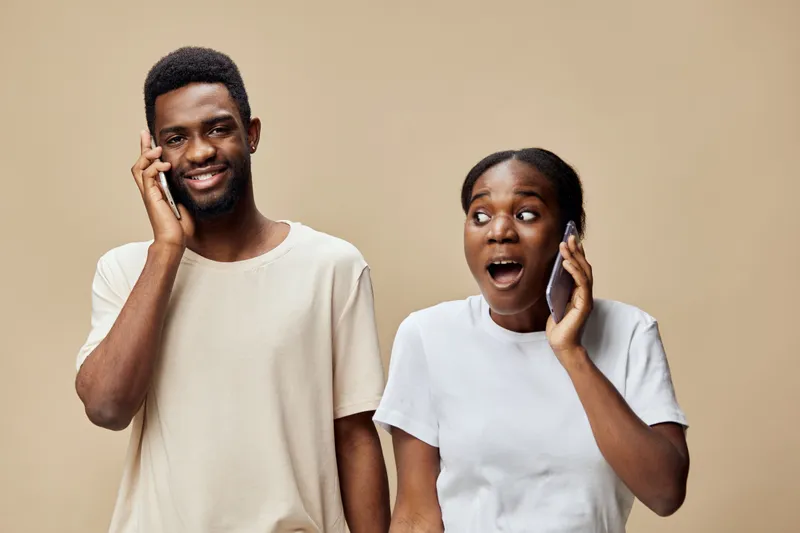 Happy couple communicating via phone with joyful expressions on a neutral background, sharing exciting news in a modern, casual style