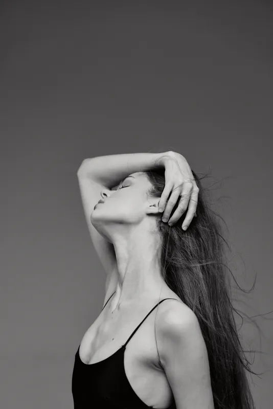 Elegant black and white portrait of a young woman with long hair posing gracefully against a neutral background.