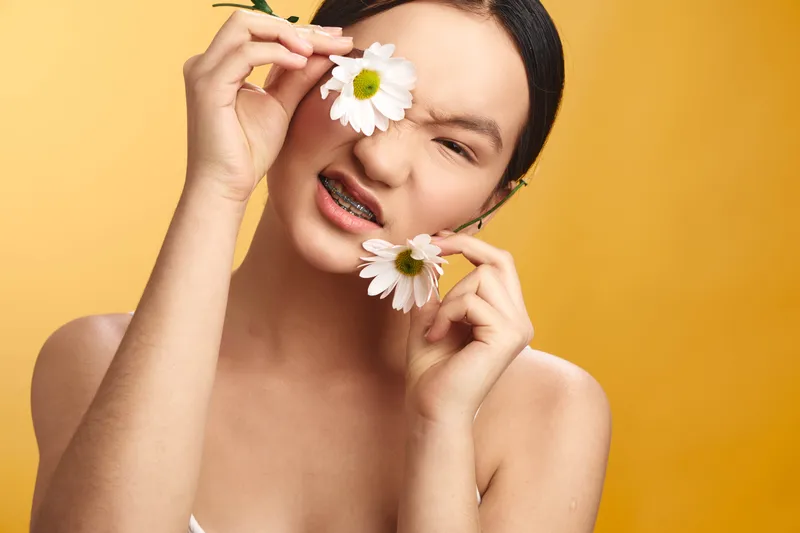 an asian woman playful and cheerful, posing with white flowers against a soft yellow background, conveying warmth, freshness, and expressive mood for lifestyle photography.