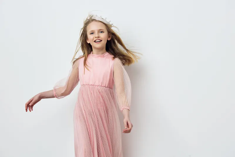 Joyful young girl in a pink dress with flowing hair, radiating happiness and innocence against a minimalist white background Perfect for children s fashion concepts