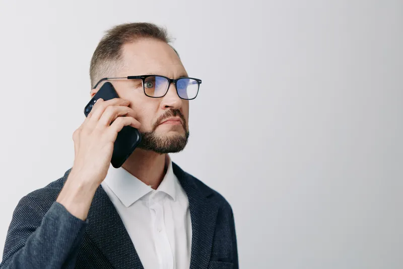 A business professional man on a call, focused and confident, captured against an isolated colored background, conveying urgency and thoughtful communication.